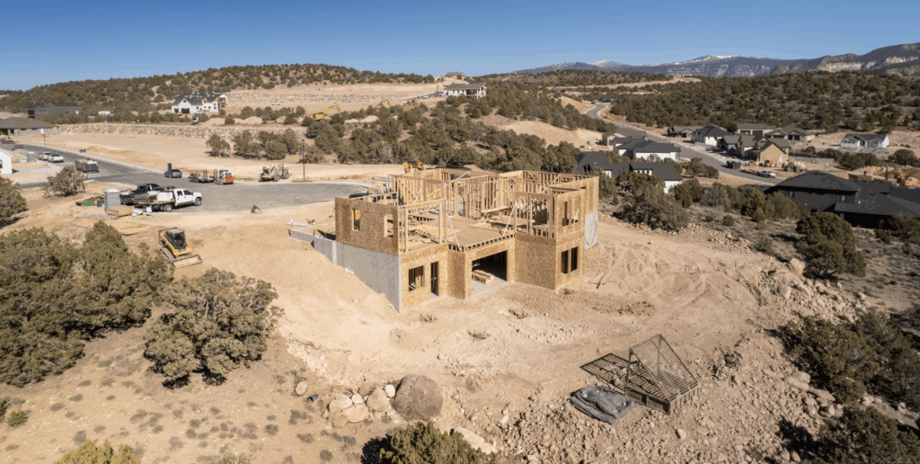 New construction home in framing phase by Archway Construction, set on a hillside with panoramic views and surrounding neighborhood development.