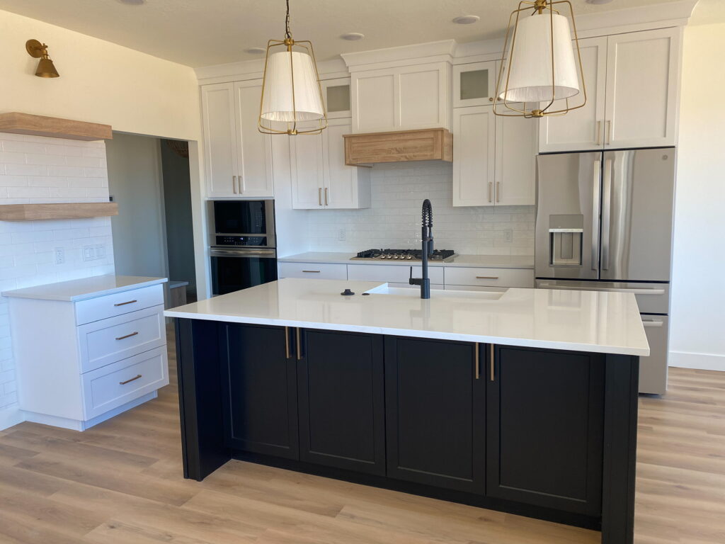Modern kitchen remodel by Archway Construction with white cabinets, black island, quartz countertops, and stainless steel appliances.